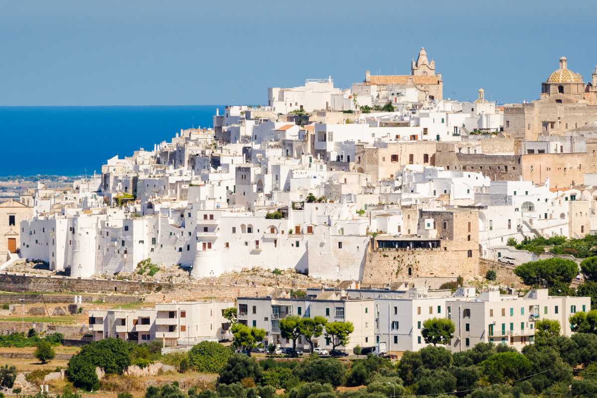 Fotografia di un vicolo bianco del centro storico di Ostuni, con arcate, fiori e dettagli architettonici tipici