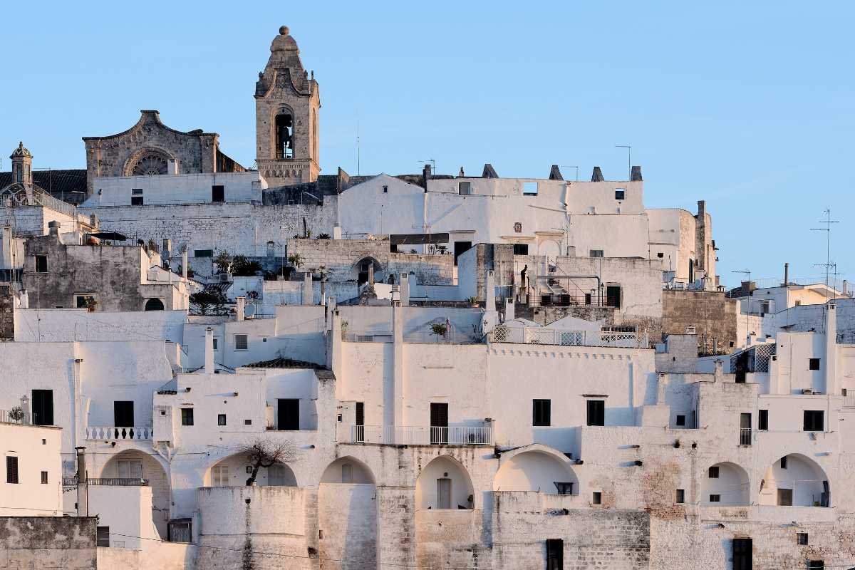 Scorcio di un vicolo bianco a Ostuni con fiori colorati e dettagli architettonici tipici