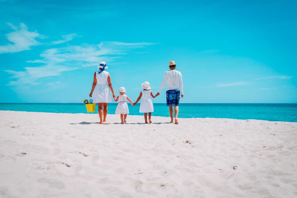 Famiglia con bambini piccoli che gioca sulla sabbia di una spiaggia vicino Ostuni, cielo sereno, mare trasparente, secchielli e palette in primo piano